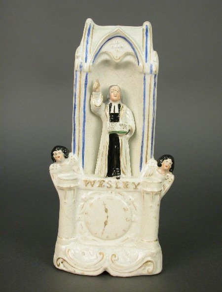 Staffordshire figure of John Wesley sta: Staffordshire figure of John Wesley standing in the pulpit on a titled gilt lined rococo base with clock face and angels to his side. His right hand is pointing in the air while left hand holds open a