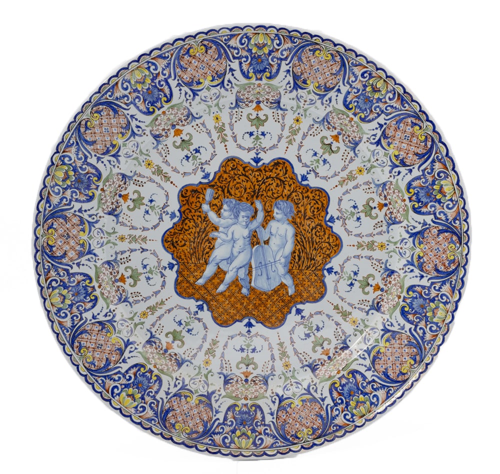 Monumental French Faience Decorative Plate by Porquier Beau Quimper: A monumental decorative plate, marked with PB monogram on underside. Heavily ornated with the finest floral decor and a trio of monochrome puttis playing musical instruments. Measuring D 1