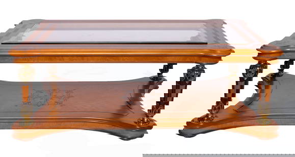 Decorated Wooden Coffee Table with Glass Centerpiece: Brown wooden coffee table with decorative trim around the border of the surface. The clear glass piece in the middle looks down onto more decorated wood below. The accent legs are carved wood with gil