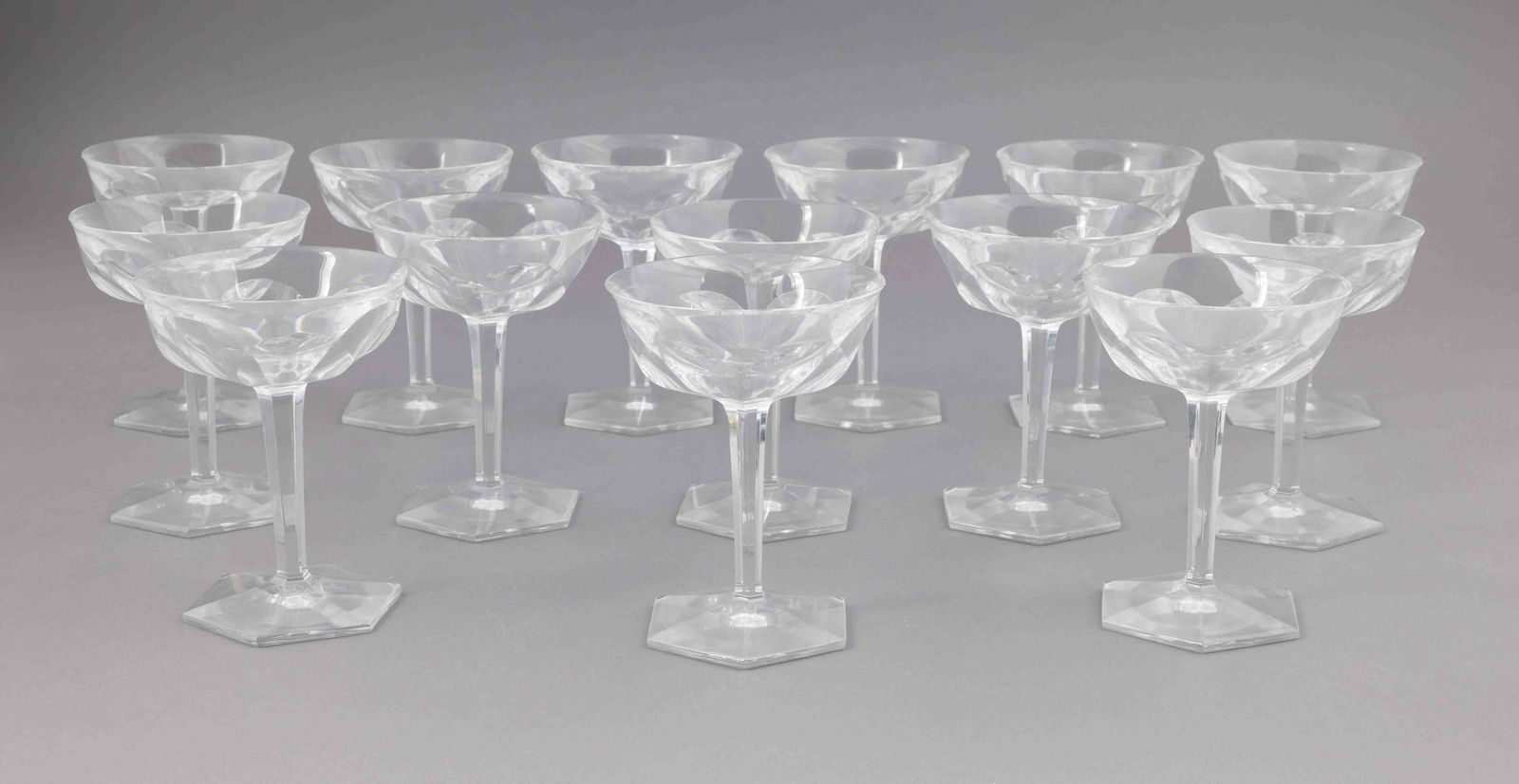 Set of Fourteen Baccarat Coupe Glasses: A set of fourteen Baccarat coupe glasses with a faceted stem and hexagonal base. They are all marked on the underside of the base with the Baccarat etching. They measure H 5.25 W 4 D 4 inches. Conditi
