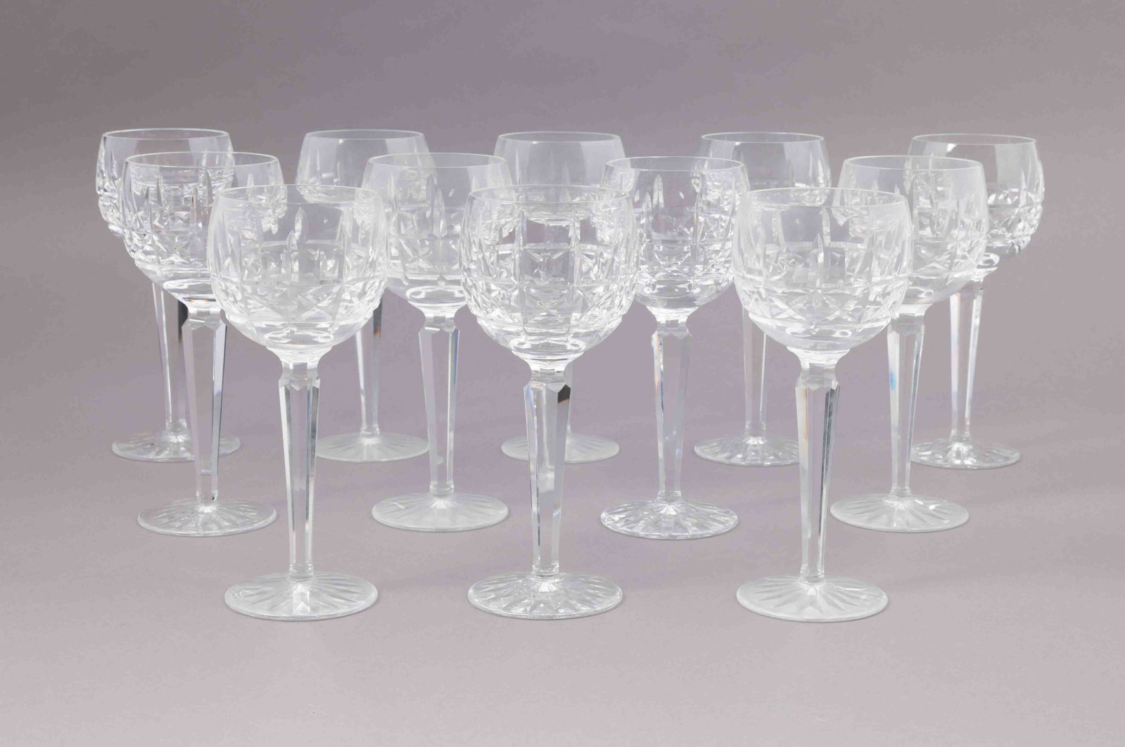 Set of Twelve Waterford Crystal Wine Glasses: A set of twelve Waterford crystal wine glasses with faceted stems and bases. They are all marked on the underside with the Waterford maker's mark. They measure H 7.5 W 3 D 3 inches. Condition: v