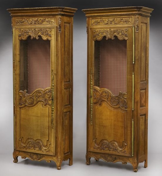 Pr. Country French carved oak vitrines: Pr. Country French carved oak vitrines with carved molded cornices over a leaf and urn carved panel, the doors with wire grill work, raised panels and foliate carvings, and standing on carved whorl fe