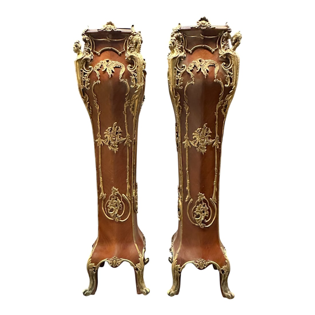 Magnificent Antique Louis XV Style Ormolu Pedestals: A pair of exceptional pedestals in Louis XV style, made of carved wood with elaborate gilt bronze fixtures featuring floral decor and four carved portraits on each corner. The top features black marbl