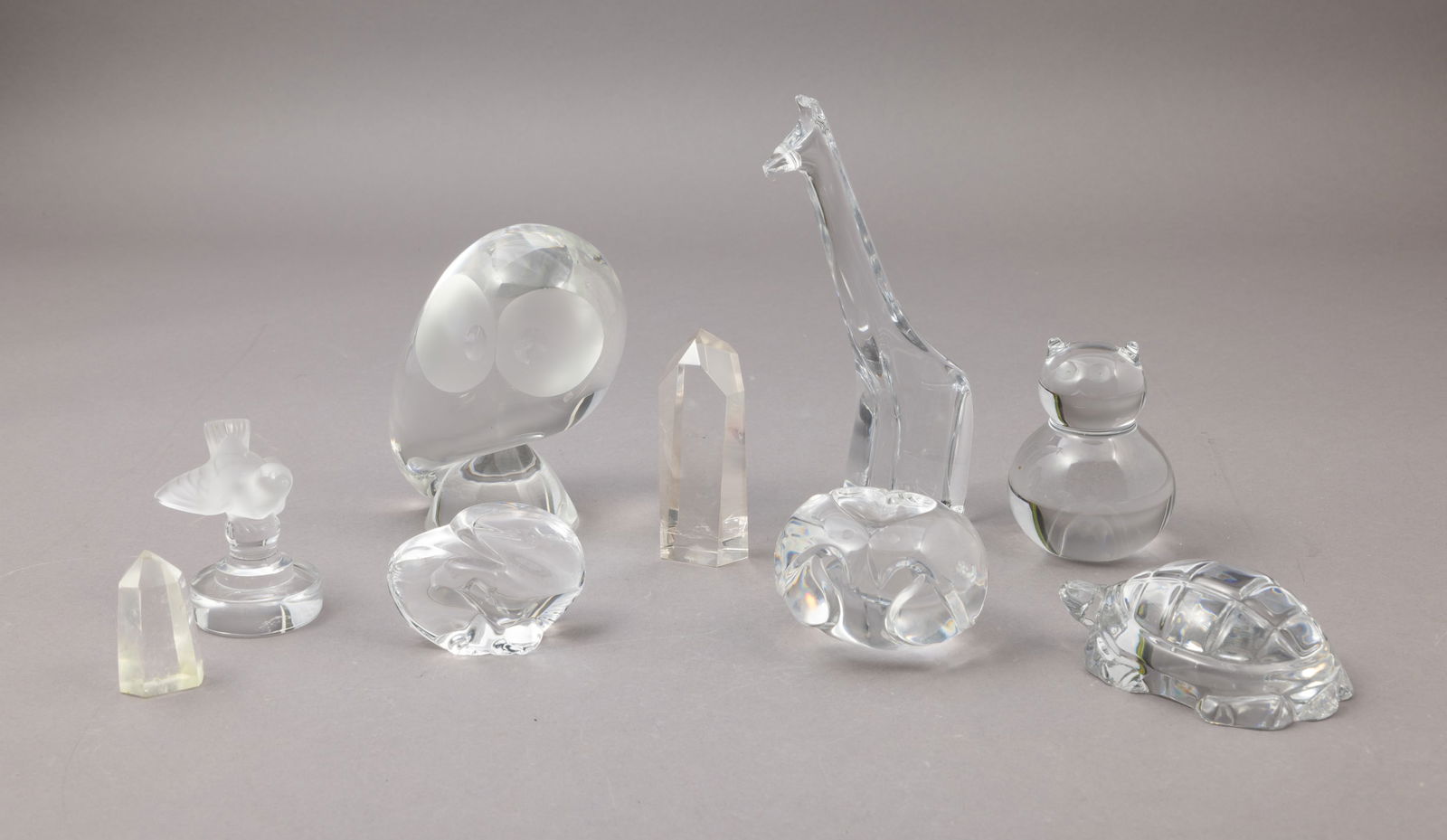 Collection of Nine Crystal Items, Lalique, Steuben: Two clear crystal obelisks measuring 4 inches x 1.5 inches and 2 inches x 1.25 inches. Good condition with minor scratching. Eagle figure measuring 2 inches x 3 inches with Steuben etched into t