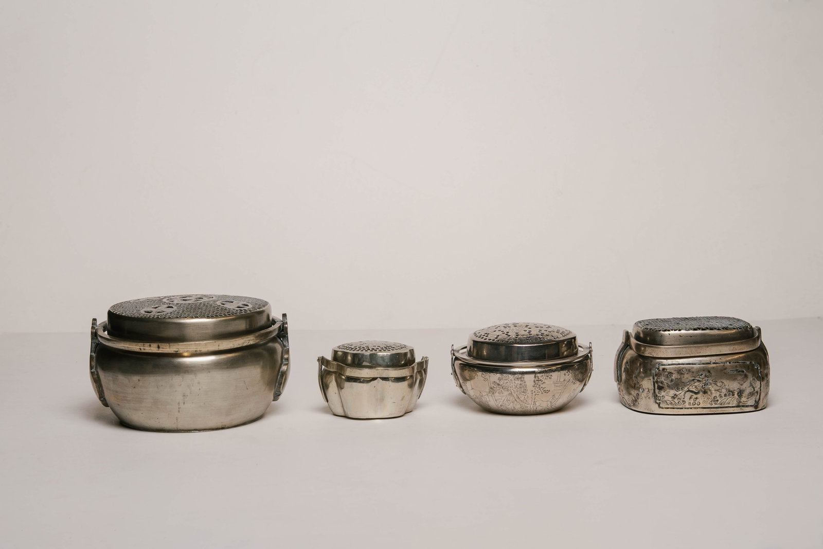 Collection of Four Vintage Chinese Handwarmers with Varying Sizes and Designs: Four Chinese Handwarmers with Varying Sizes and Designs. Smallest to Largest: The smallest's top has a floral center piece, and a base with six sections. The second smallest has a floral top and sides