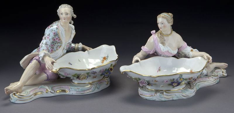 Pr. large Meissen figural sweet meat dishes: Pr. large Meissen figural sweet meat dishes modeled with an elegant lady to one, the other with a gentleman. Cross swords mark in blue underglaze and incised numbers. Larger: 7"H x 13"L, Circa - 20th
