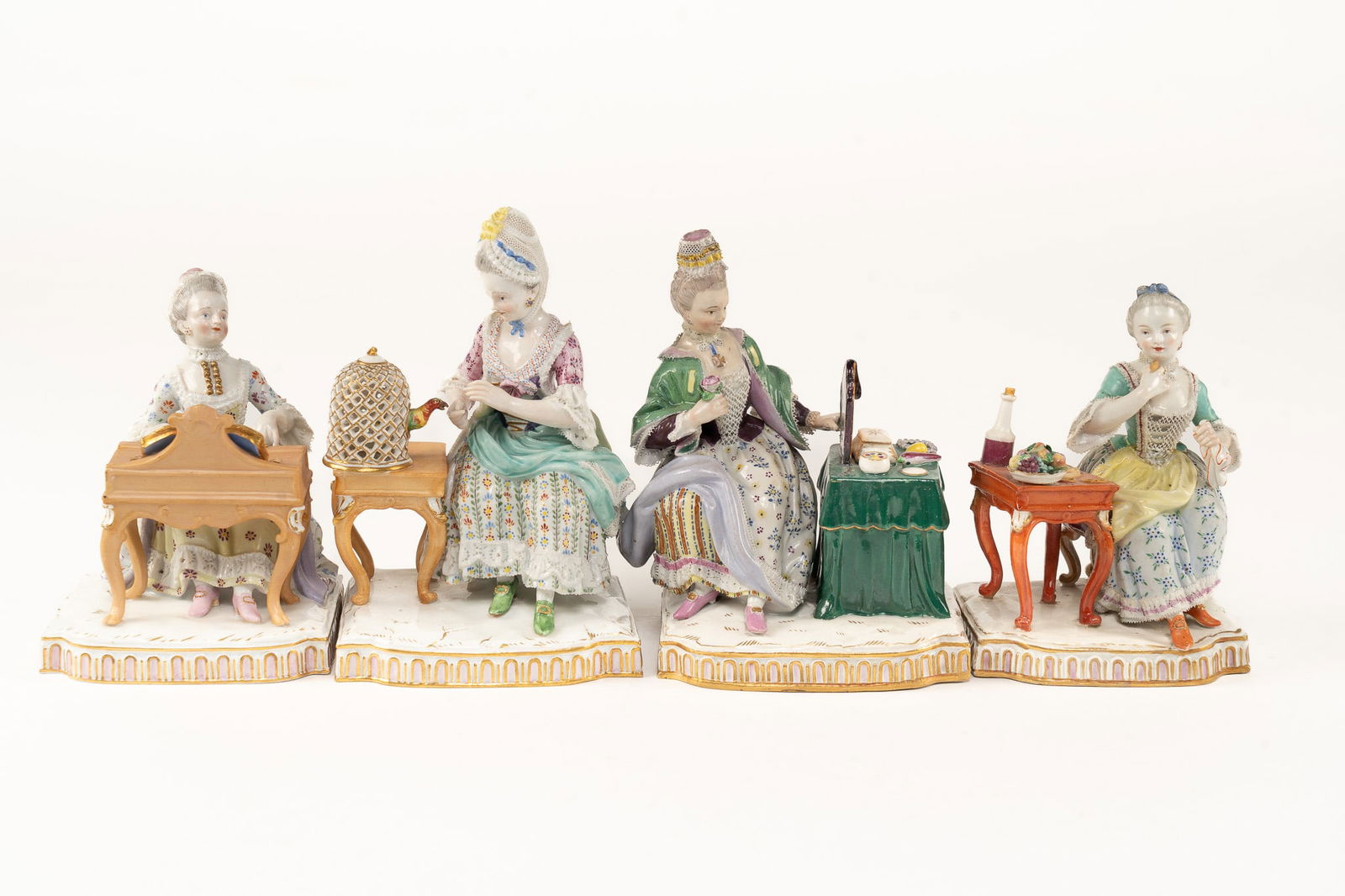 Lot of 4 Antique Meissen Ladies: A group of ladies each seated at a table. One putting on makeup, one attending to her parrot, one eating, and one playing a piano. Each signed with the blue crossed sword logo. Measuring approx