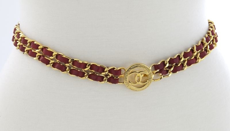 Chanel burgundy leather and gold tone linked belt: Chanel burgundy leather and gold tone linked belt with double chains connecting at the center with a logo clasp. Measuring 27.25" L. Note: This piece is part of a capsule collection offered by The Vin