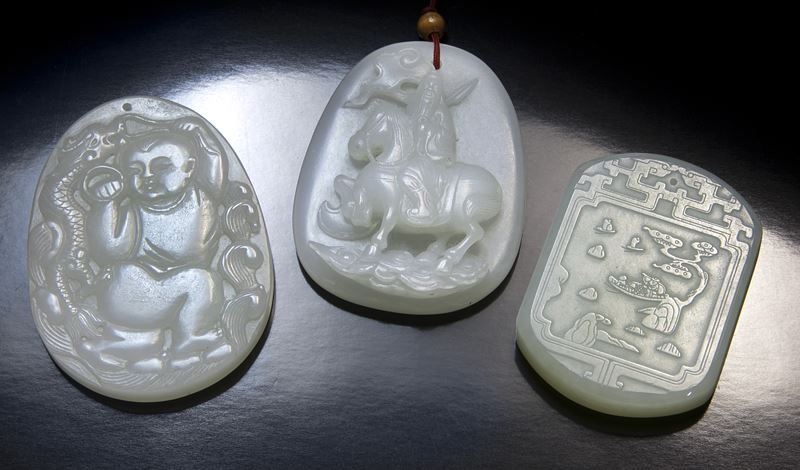 (3) Chinese carved jade pendants.: (3) Chinese carved jade pendants. (1) of oval form, depicting a bearded general in armored suit, riding on his horse in high relief, the verso with two archaistic chilong in low relief; (1) of oval fo