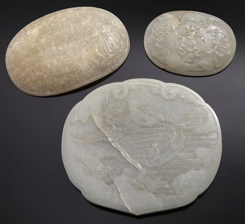 (3) Chinese Qing carved jade plaques: (3) Chinese Qing carved jade plaques of various forms and tone, carved in low relief with Buddhist auspicious symbols and figures in riverscapes, as ruyi heads. Largest: 5.25" (13cm), Circa - 18th - 1