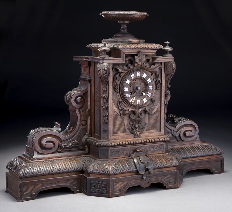 Black Forest carved wood clock: Black Forest carved wood clock surmounted by a carved urn, the dial surrounded by leafy scrolls, on a carved wood breakfront plinth; with a circular brass time and bell strike movement with pendulum. 