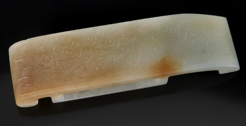 A Chinese white and russet jade sword: A Chinese white and russet jade sword scabbard slide carved with C-scroll motif and stylized taotie mask. Provenance: The first, ex-collection of a prominent Northern California collector. 1"H x 3.75"