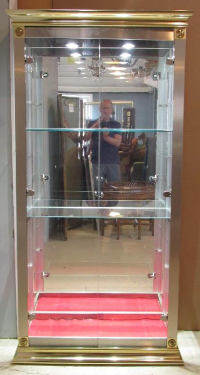 Modern Maison Jansen Style Illuminated Vitrine: Glass encased with Hollywood Regency style trim. Bottom inset shelf missing. Brass and Chrome 40" X 18" X 80"