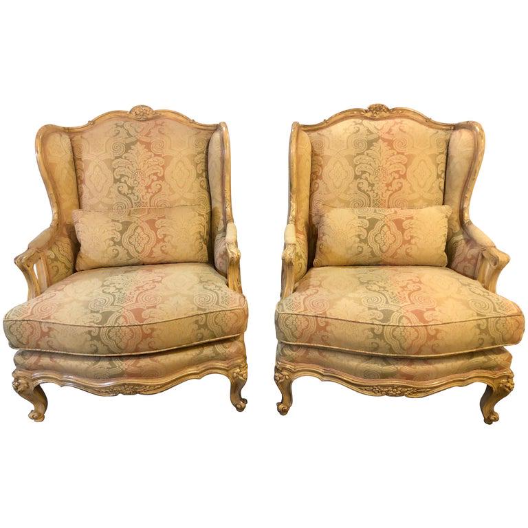 Pair of Palatial Louis XV Bergere Chairs: Distressed wingback or bergere chairs, finely carved with roses, leaves, and vines on painted frame. Hollywood regency style. 42" x 30.5" x 31" Seat height: 19.5"