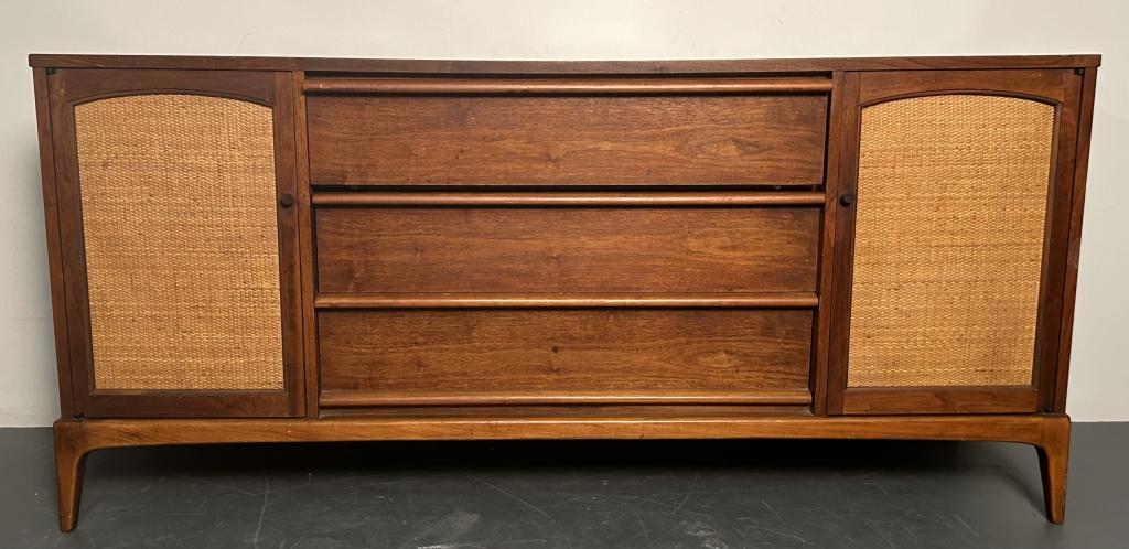 Mid Century Modern Entertainment Console: Mid Century Modern Entertainment Console. Rattan accents on side doors, three drawers in the center. Some staining/chips (pictured). Height 31 Inches, Width 66 Inches, Depth 18 Inches.