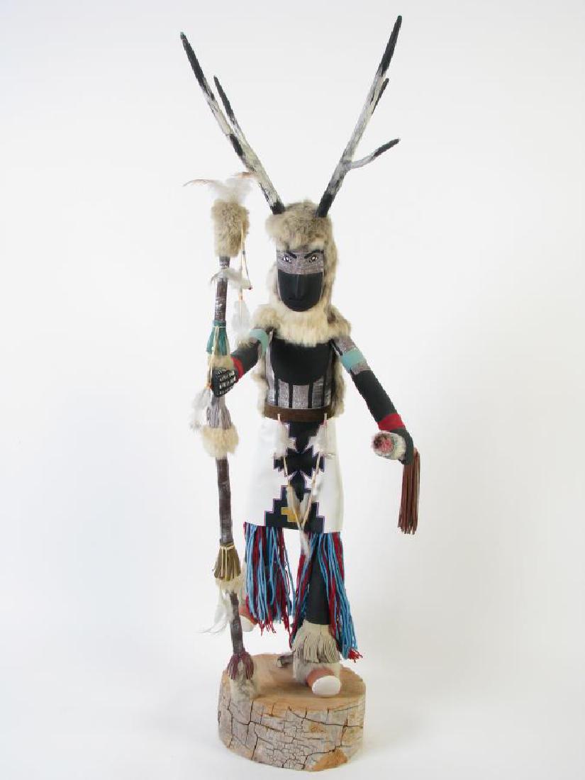 Monumental Cottonwood "Deer Man" Kachina: Monumental Cottonwood "Deer Man" Kachina, the deer man dances to increase his kind for plenty to eat for the future, depicting figure holding a staff and rattle, two tone painted face with fur headdre