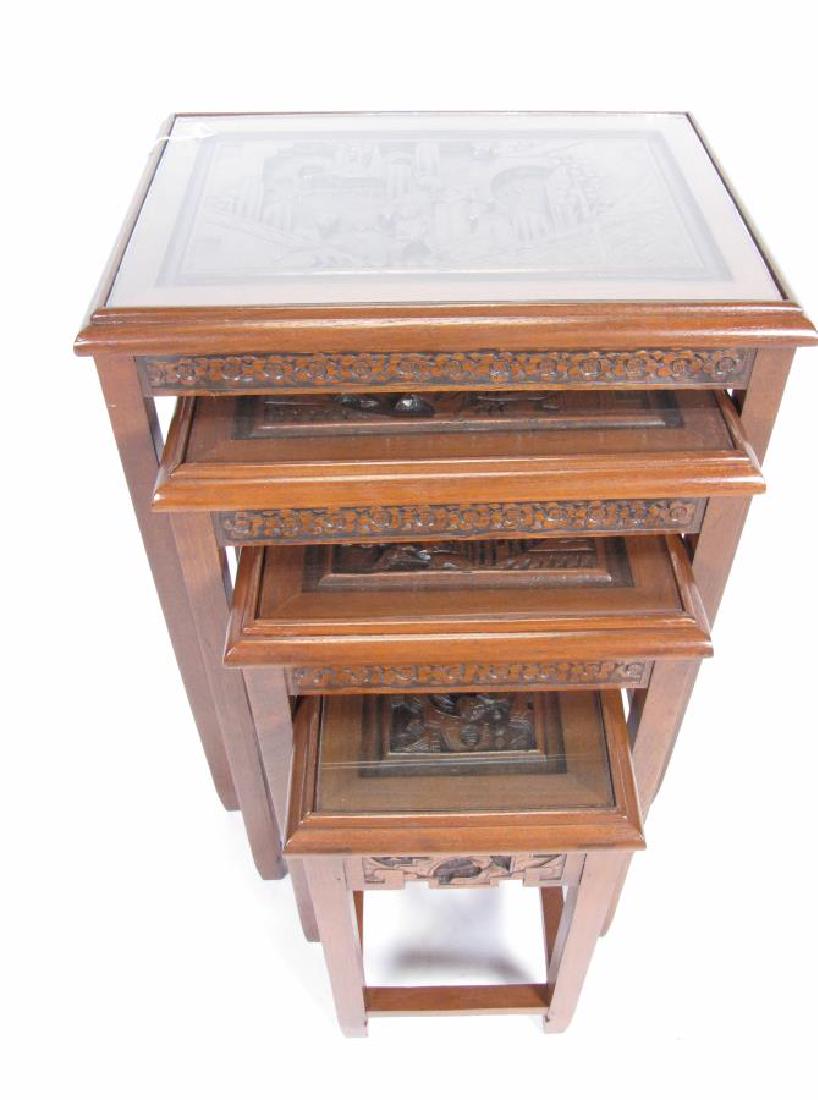 Four Piece Set of Nesting Tables: A four-piece set of mahogany, carved nesting tables, with each table has recessed scenic carving with figures, largest table is 20 x 24 x 26.5"h, each with glass top