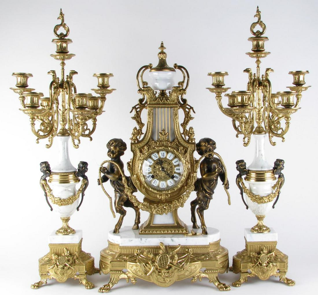 Franz Hermle Clock and Garniture: An Italian Baroque style figural marble and gilt metal clock and garniture, depicting two opposing Faun holding floral decorated rope, footed base with white marble top, Roman numeral dial, seven-ligh