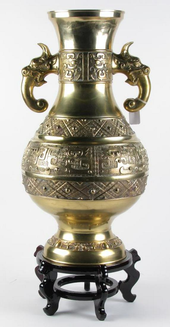 India Brass Floor Vase on Wood Stand: An India brass floor vase urn style vase with mythical creature handles, Greek key decoration, 23.5" high, on wood carved stand