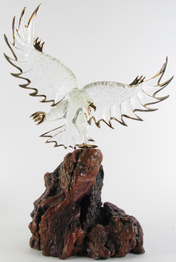 Glass Bald Eagle on Driftwood Base: A glass bald eagle sculpture, depicting clear glass bald eagle, with spread wings, gold decorated eyes, beak, talons and wing tips, on natural driftwood base, unsigned, 16" x 8" x 22.75"
