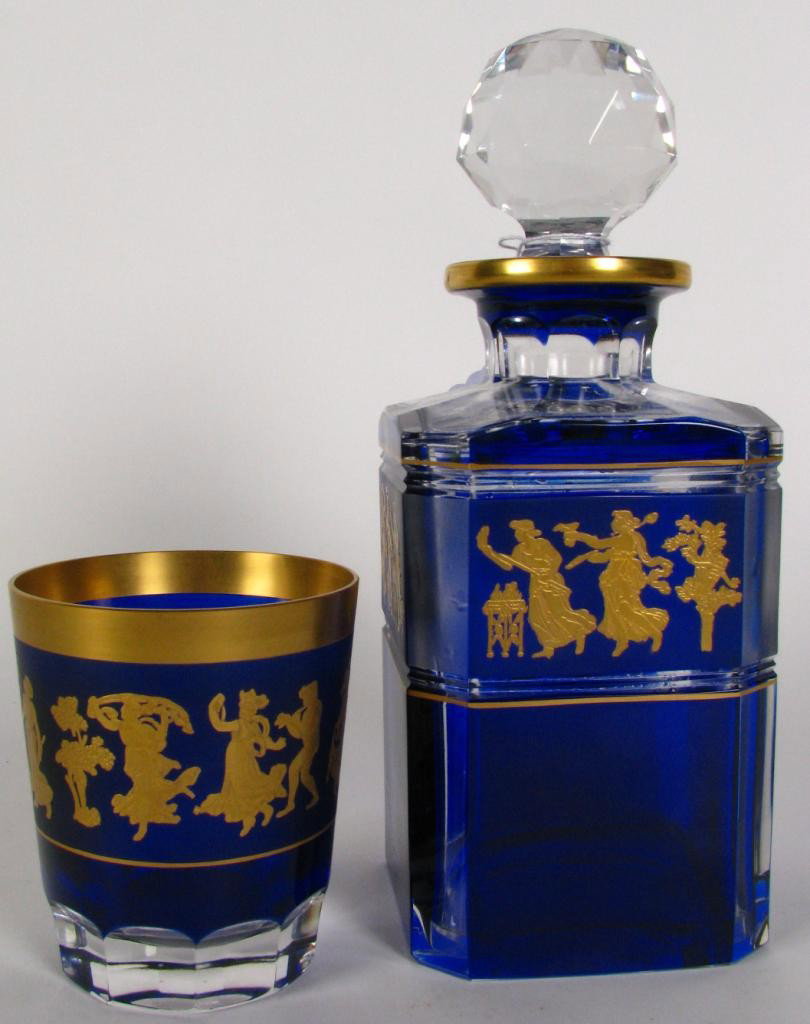 Two Pieces Val St Lambert Cobalt to Clear: Two pieces of Val St Lambert crystal, both depicting celebrating figures in classic attire, cobalt cut to clear with gold trim, tumbler is 4" high with paper label, decanter with stopper is 10" high