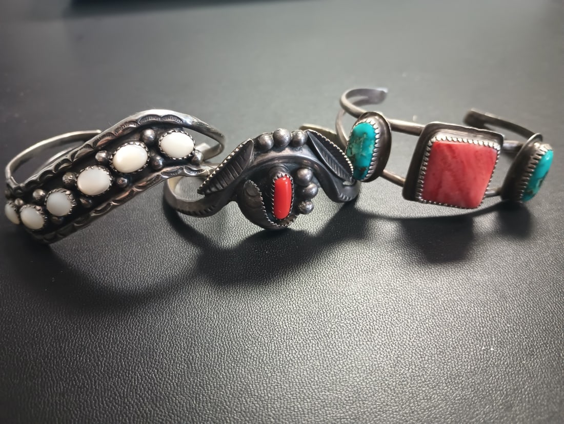 (3) Silver Native American Cuff Bracelets: (3) Native American cuff bracelets, including one with turquoise and orange spiny oyster, marked 'sterling' and marked JA Fragua, one with coral bead, unmarked, and one with mother-of-pearl buttons an