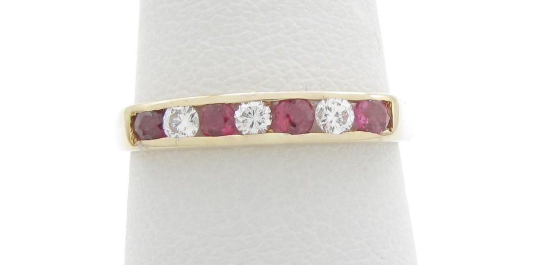 14K Yellow Gold Ruby and Diamond Band Ring: A 14K yellow gold band ring featuring four round brilliant cut rubies and three round brilliant cut diamonds, each approximately .08ctw, channel set. Ring size approximately 5.6. Band width 2.89. Ring