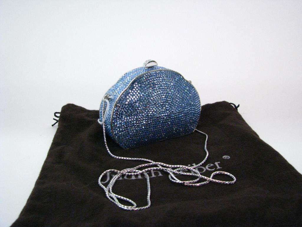 Judith Leiber Blue Crystal Minaudiere Purse: Judith Leiber blue crystal minaudiere evening purse. Purse has scallop shape at top with clear crystal clasp. Silver tone hardware. Interior is lined with silver leather. Attached silver twist shoulde