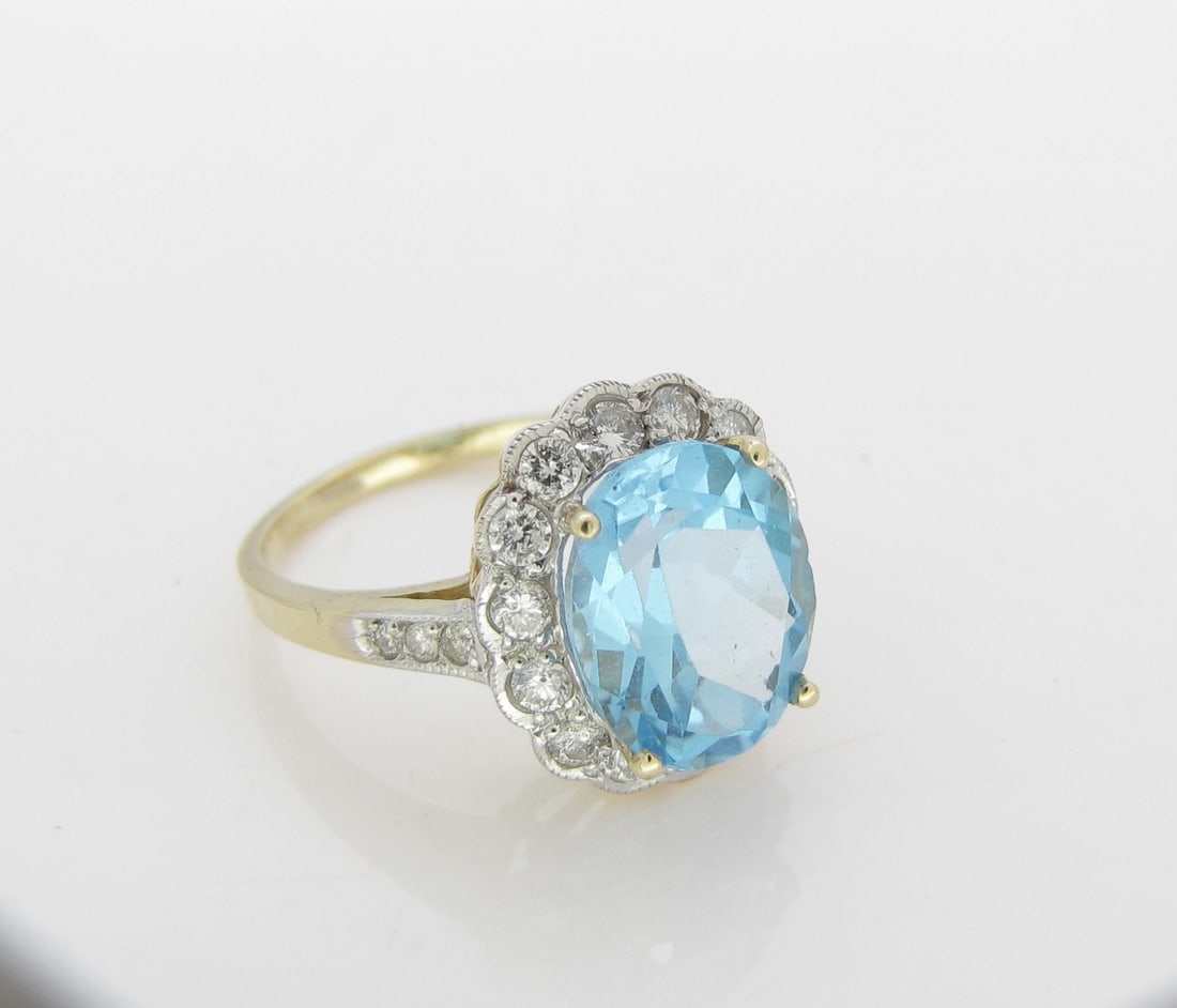 14K WG/YG Blue Topaz and Diamond Ring: A 14K yellow gold ring featuring a 10.8mm x 8.7mm center blue topaz, in a white gold mount with yellow gold prongs, surrounded by fourteen round brilliant cut diamonds, each weighing approximately