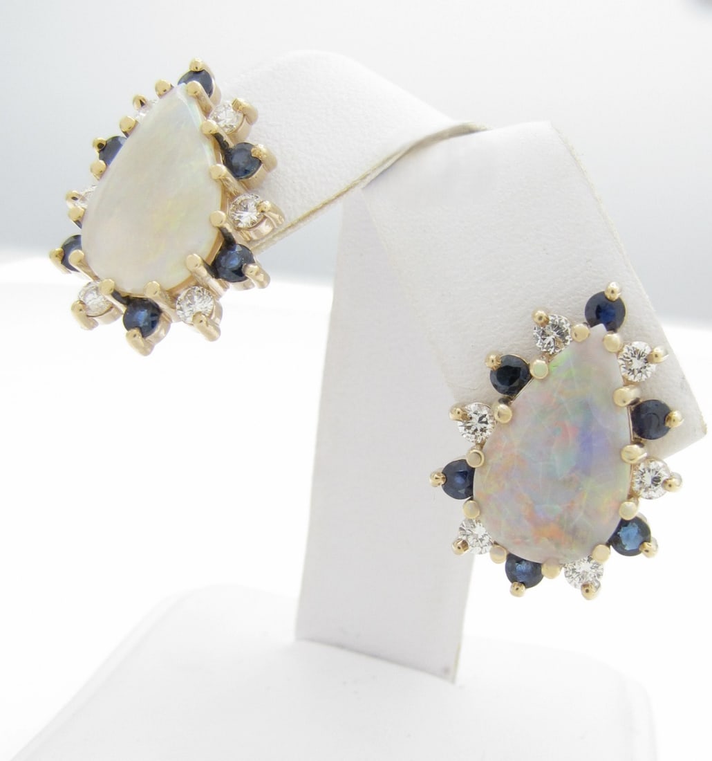 14K Yellow Gold Opal, Diamond, Sapphire Earrings: A pair of 14K yellow gold stud earrings, each containing a 14mm x 9mm pear shaped opal surrounded by six sapphires and six earrings, each approximately .03ct. Total diamond weight approximately