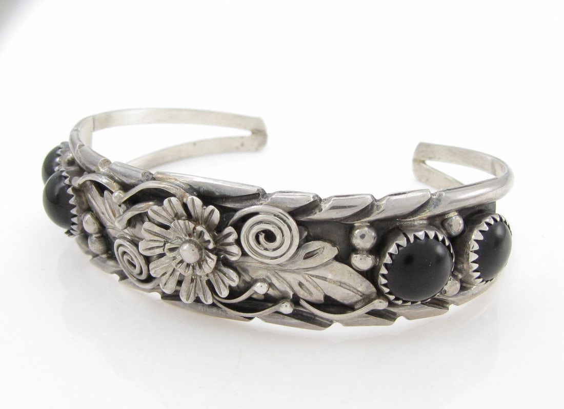 Fred Harvey Sterling Onyx Floral Cuff: A Fred Harvey sterling silver floral embossed cuff bracelet with four round approximately 8mm cabochon onyx. Interior circumference approximately 6.5". Approximately 17mm wide at front and 6mm at