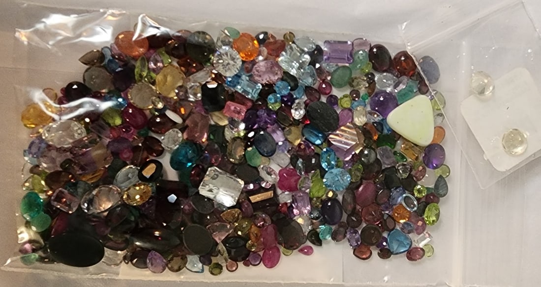 Bag of Loose Gemstones: A bag of loose gemstones including stones with the appearance of opal, mother of pearl, garnet, blue topaz, emerald, amethyst, aquamarine, peridot and more. In varying sizes (and shapes) up to