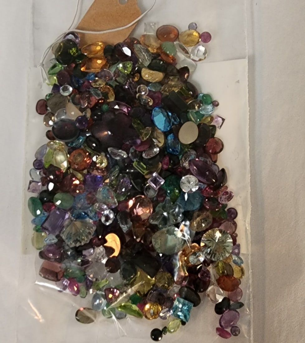 Bag of Loose Gemstones: A bag of loose gemstones including stones with the appearance of opal, mother of pearl, garnet, blue topaz, emerald, amethyst, aquamarine, peridot and more. In varying sizes (and shapes) up to approxi