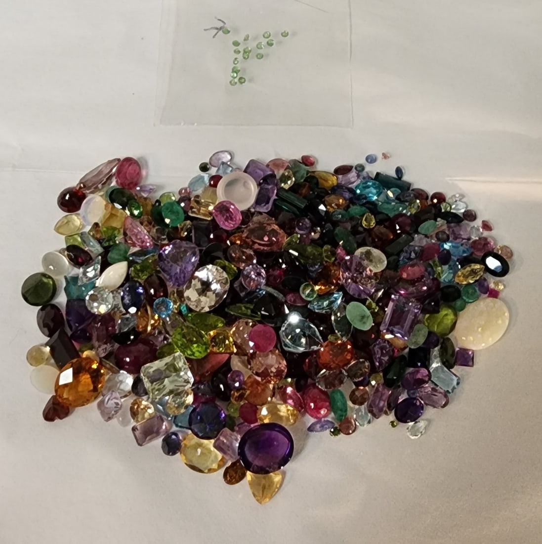 Bag of Loose Gemstones: A bag of loose gemstones including stones with the appearance of opal, mother of pearl, garnet, blue topaz, emerald, amethyst, aquamarine, peridot and more. In varying sizes (and shapes) up to