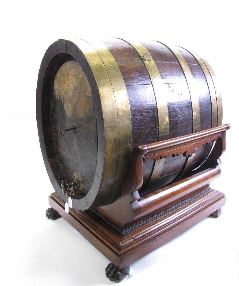 Antique Wine Barrel Safe: Antique wine barrel safe, consisting of brass banded, hand hammered wine barrel with hinged door, revealing fitted interior, resting on a carved walnut cradle style base with paw feet, label affixed t