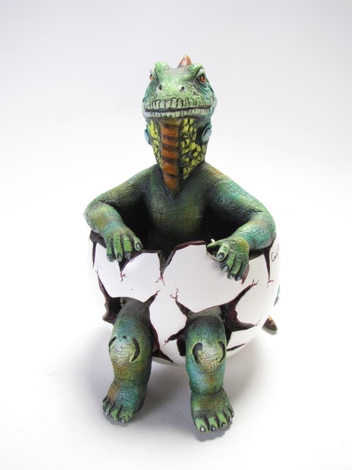 Carlos and Albert Iguana in Egg Sculpture: Carlos and Albert Iguana in Egg Sculpture, depicting a iguana sitting inside an egg with its legs and tail sticking out, hand painted green body with orange and yellow around the head and neck, limite