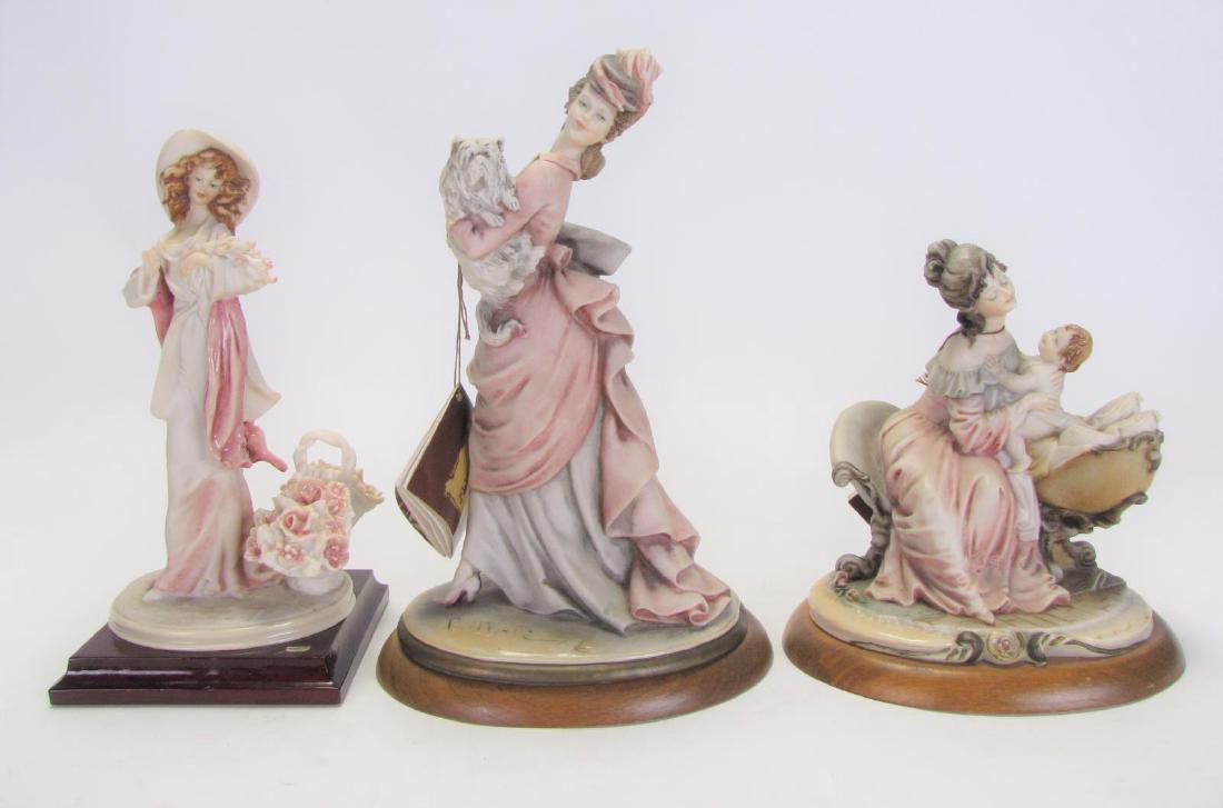 Three Bruno Merli Resin Figures: Three Bruno Merli Resin Figures, one depicting mother laying child in basinet, signed in cast "B. Merli, 1989-B. Merli" with Capodimonte hallmark, mounted on oval wooden base; one depicting maiden in