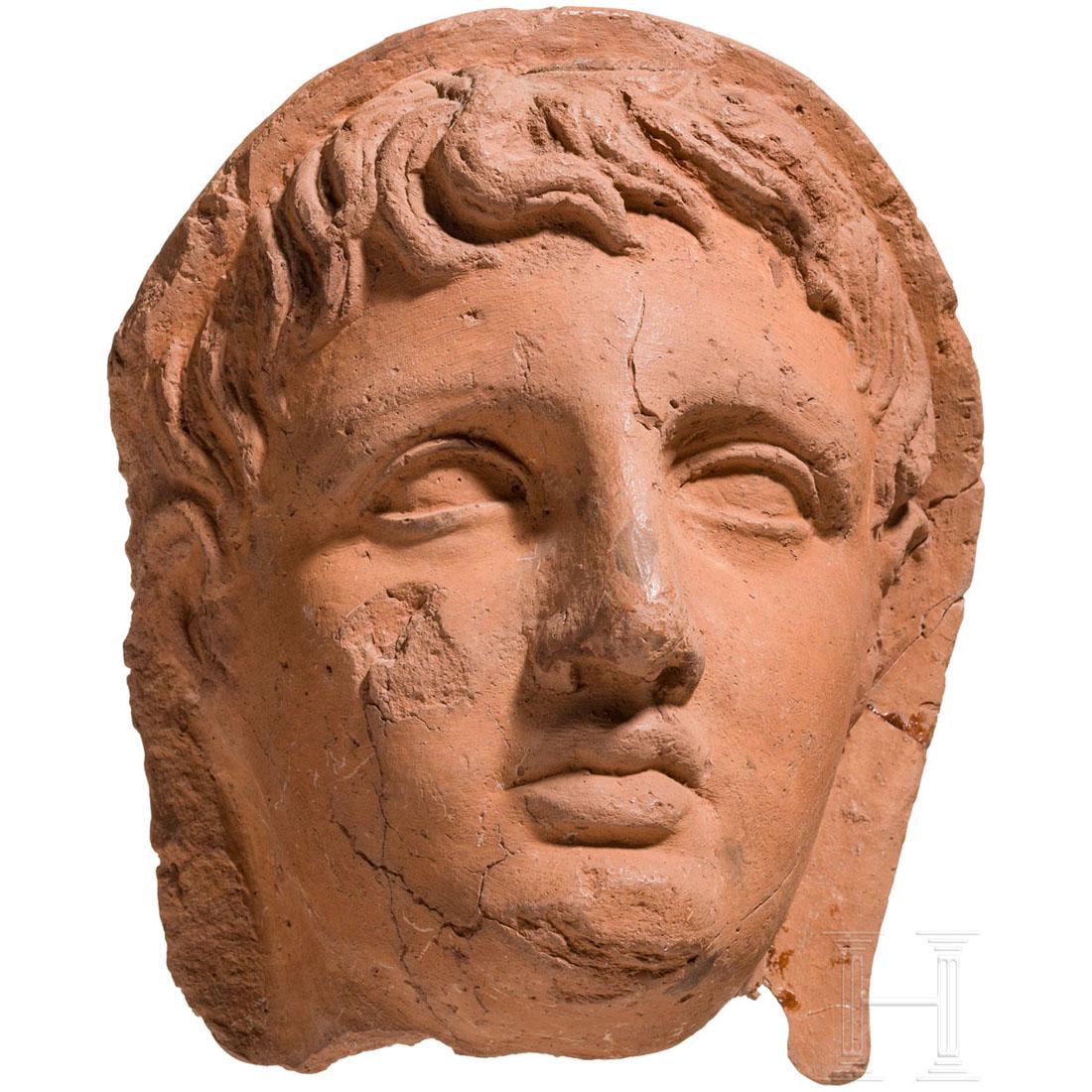 An Etruscan votive head of a young man, 2nd half of the: Life-sized terracotta mask of a young man with a cloth over his head (lat. capite velato). The neck is broken. Bumped at left edge, broken and glued at right. Small missing chip under the right eye. T