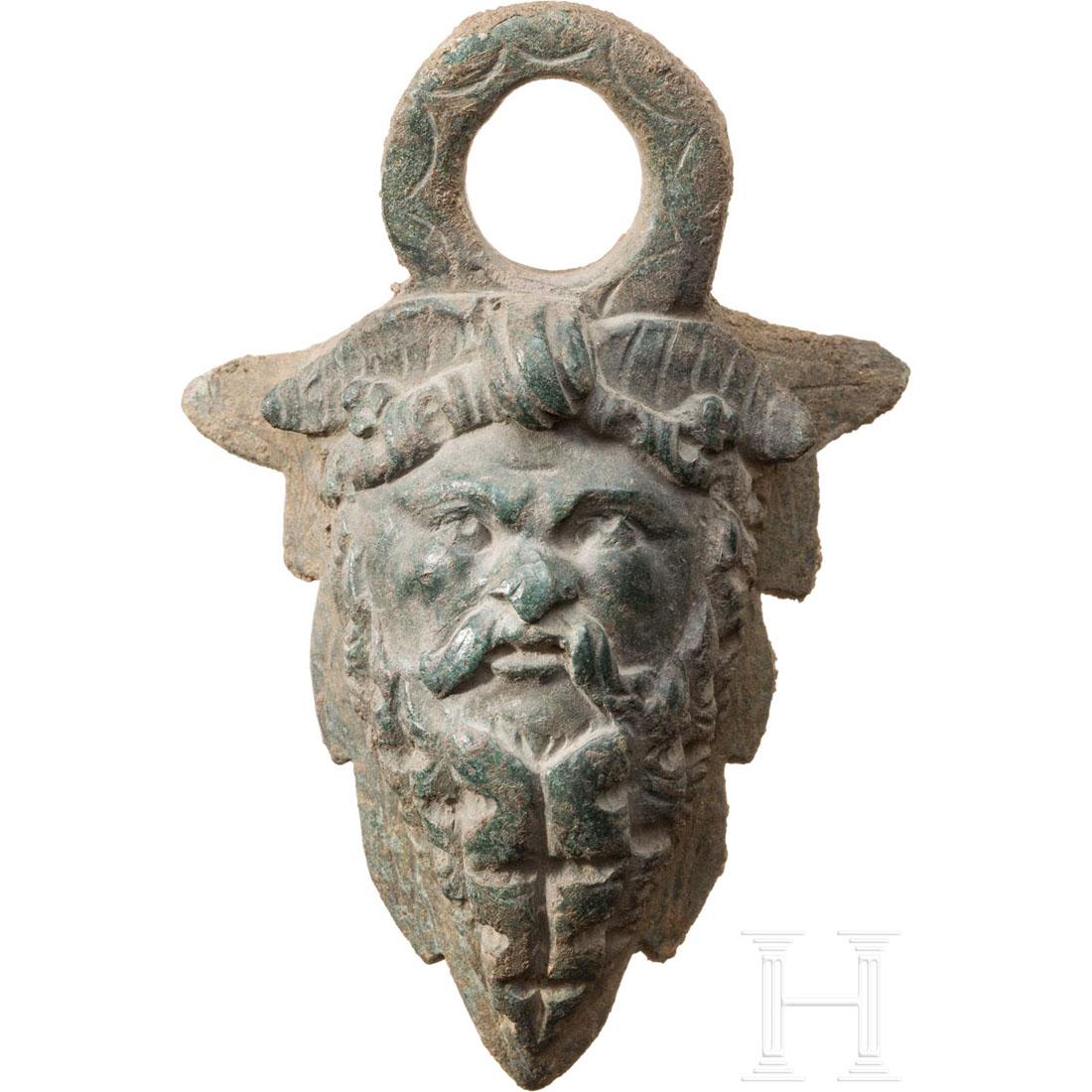 A Roman satyr appliquÃ© from a bronze vessel, 1st - 2nd: Large bronze loop for a handle, with bearded satyr head. The mask is slightly bend on the back, a hint that it was attached to a larger bronze vessel. Bronze with beautiful dark green patina. Intact. 