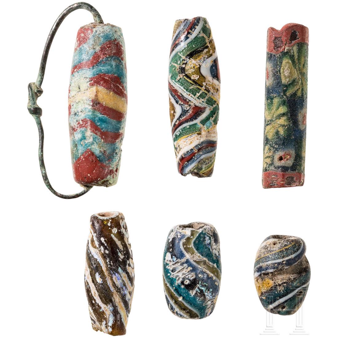 Six biconical and cylindrical beads, Eastern: A Roman-Egyptian hexagonal-cylindrical pearl made of faceted mosaic glass. And five biconical polychrome beads of banded mosaic glass, one of them with bronze wire suspension. Lengths 1.3 to 2.8 cm. P