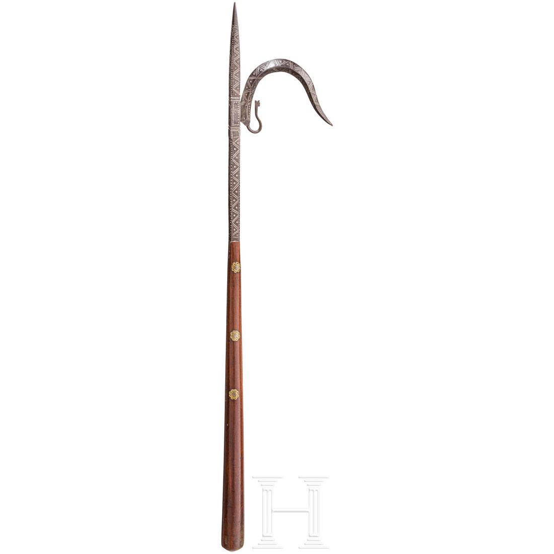 An Indian ankus, circa 1900: Schmiedeeiserne Konstruktion mit geometrisch punzierter Vierkantspitze, seitlichem Haken und mittig durch Eisen verstÃ¤rktem, konischem und dreifach vernietetem Holzschaft. LÃ¤nge 69 cm. Zustand:I