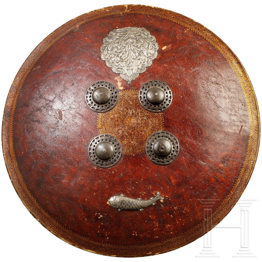 A leather shield with silver fittings, India, 19th: GewÃ¶lbter, beidseitig kupferfarben gefasster Rundschild aus dickem Rohleder. Mittig und umlaufend am Rand goldfarbenes Floraldekor. Zwei vernietete, halbplastisch getriebene Silberbleche (Fisch und