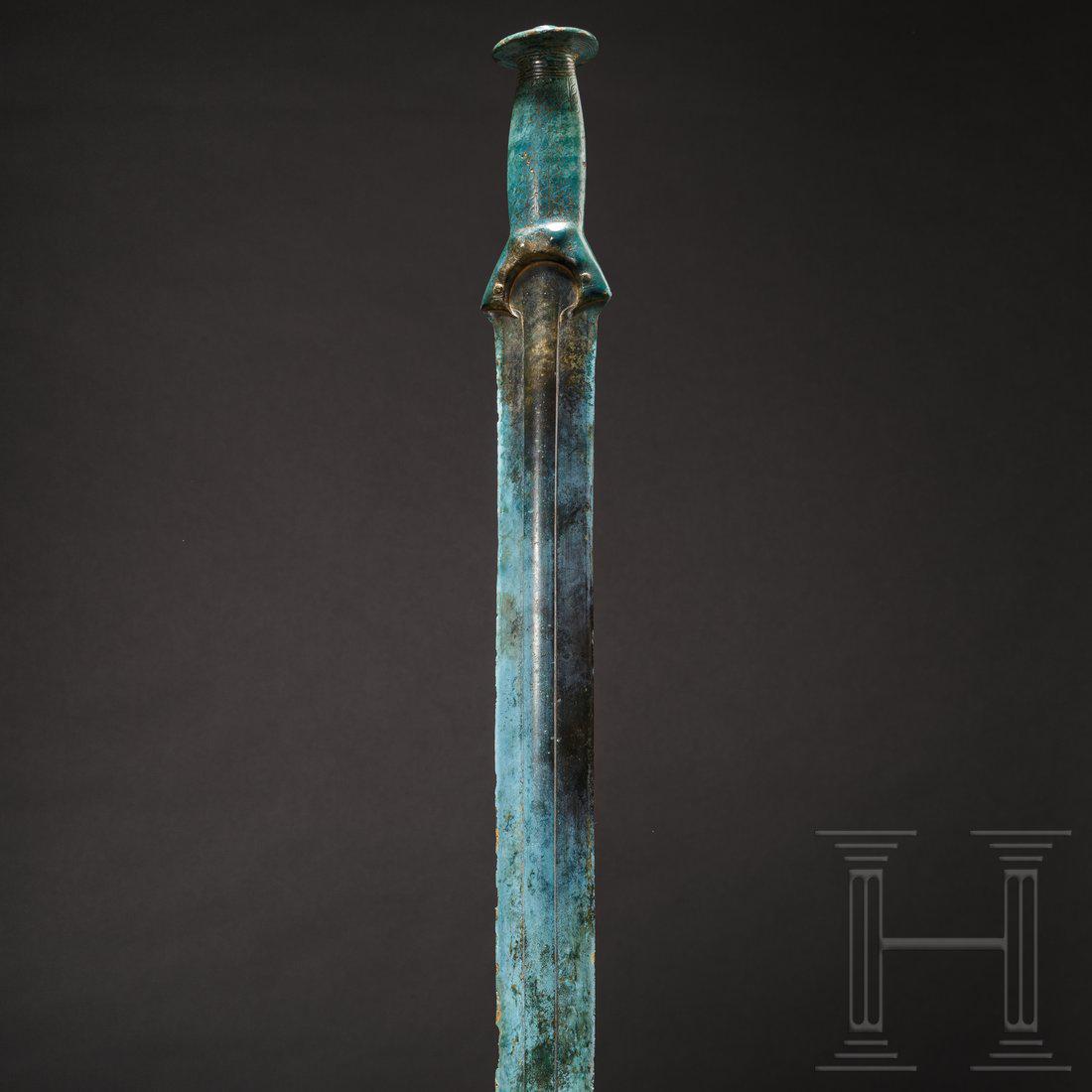 A German bronze sword of the Riegsee type, 1300 â€“: A beautifully preserved bronze sword with long, narrow blade. With wide, raised central ridge. The flattened hilt is decorated with rows of engraved braided bands. With oval disc-shaped knob. Slight b