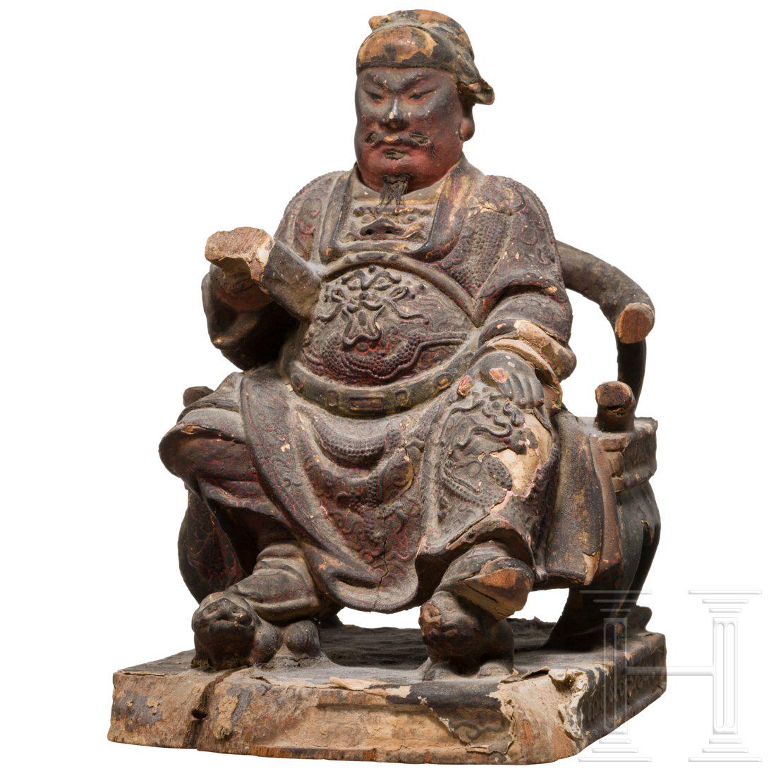 A Chinese carved and painted sculpture of a sitting: Carved and painted wood. Partly chased and covered in paper or fabric. Backside with old collecting label. Rests of gilding. Smaller pieces lost. Socket chipped. Dimensions 18 x 12,5 x 14 cm. Attentio