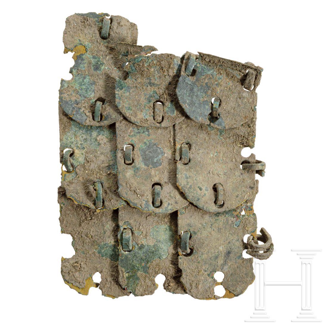 A fragment of a Roman lorica squamata, 2nd - 3rd: Segment of a lorica squamata consisting of nine broad bronze lamellas connected by wire rings. Two lamellas broken at the top. With dark-green patina. Length 6.3 cm. Provenance: From a private collect
