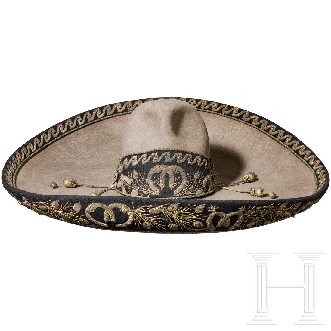 A Mexican sombrero with silver embroidery, 19th century: A wide-brimmed sombrero mexicano in strong, pale grey felt. The upturned edge all the way round and the lower half of the crown adorned with black, silver-embroidered trim. The crown featuring the fou
