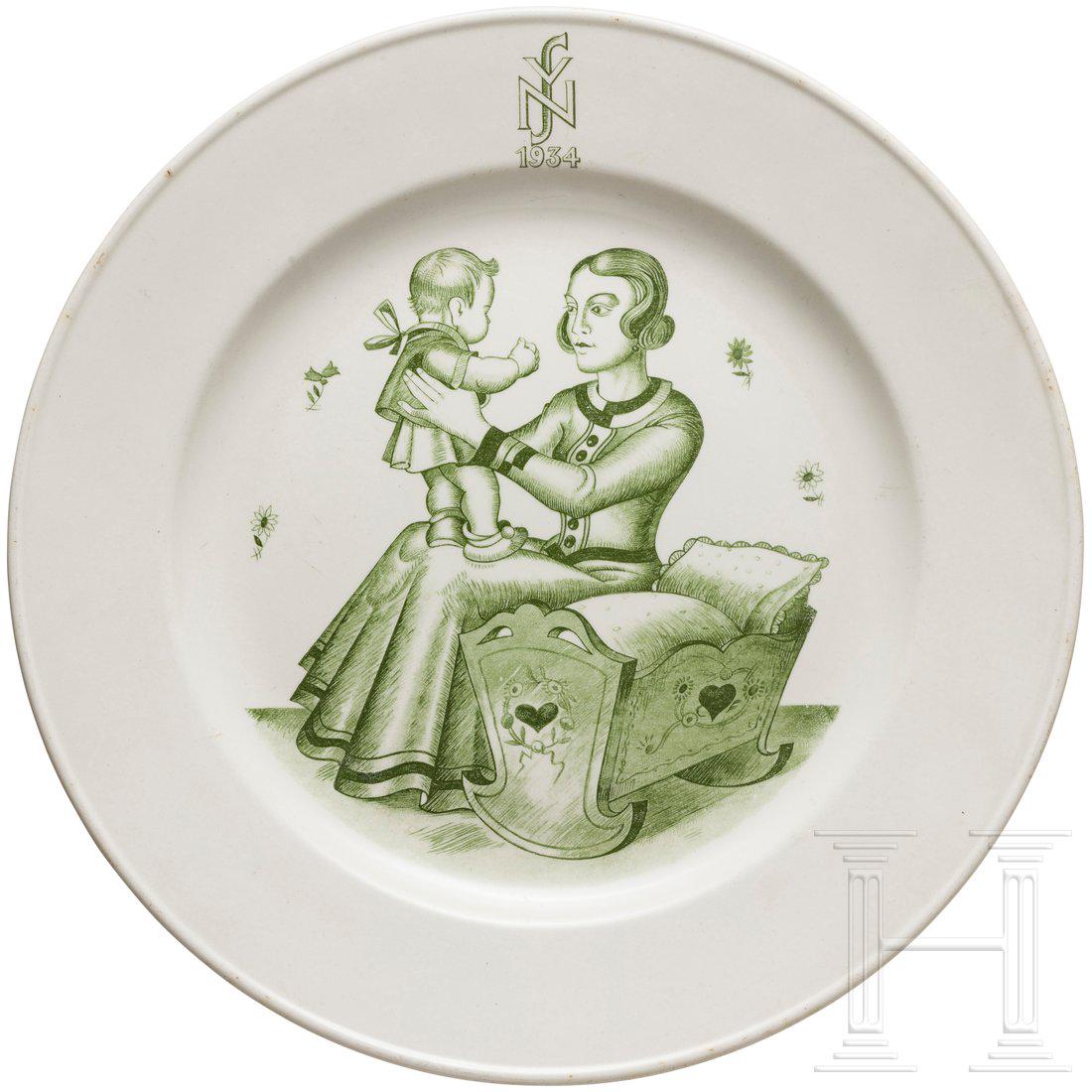 NSV-Wandteller, Gau 10 Hessen-Nassau: Glasierter, weiÃŸer Steingutteller. Motiv und Schrift in MoosgrÃ¼n. Motiv: Mutter, auf dem SchoÃŸ ein stehendes Kind haltend, daneben eine Wiege. Im Hintergrund vier kleine BlÃ¼mchen. Am Telle
