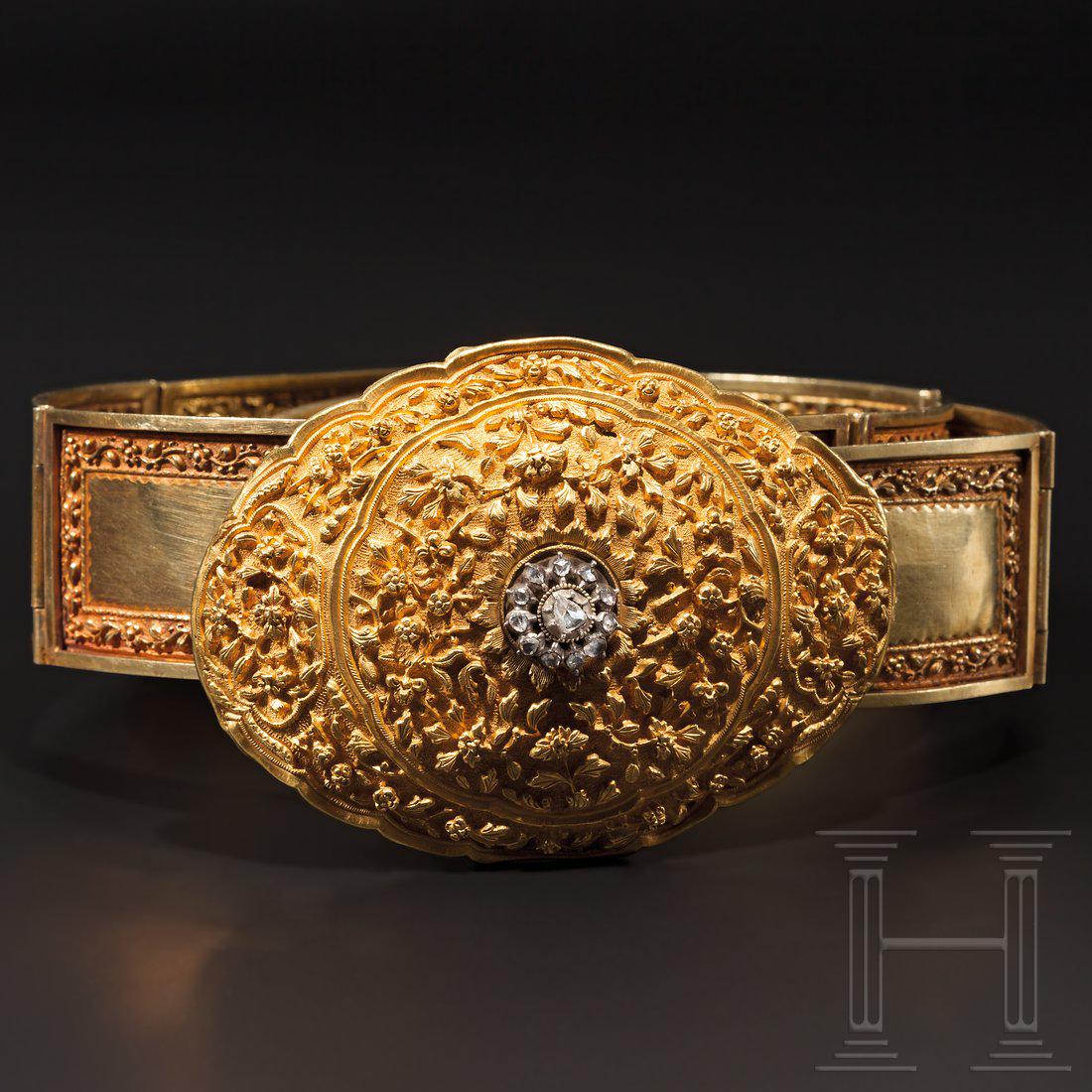 A decorative diamond-studded Indian gold belt, 1st half: Belt consisting of ten rectangular, hinged gold parts (over 21 carat), each with florally embossed framing, reinforced edges and lateral closing hooks. The very finely embossed, oval buckle with flora
