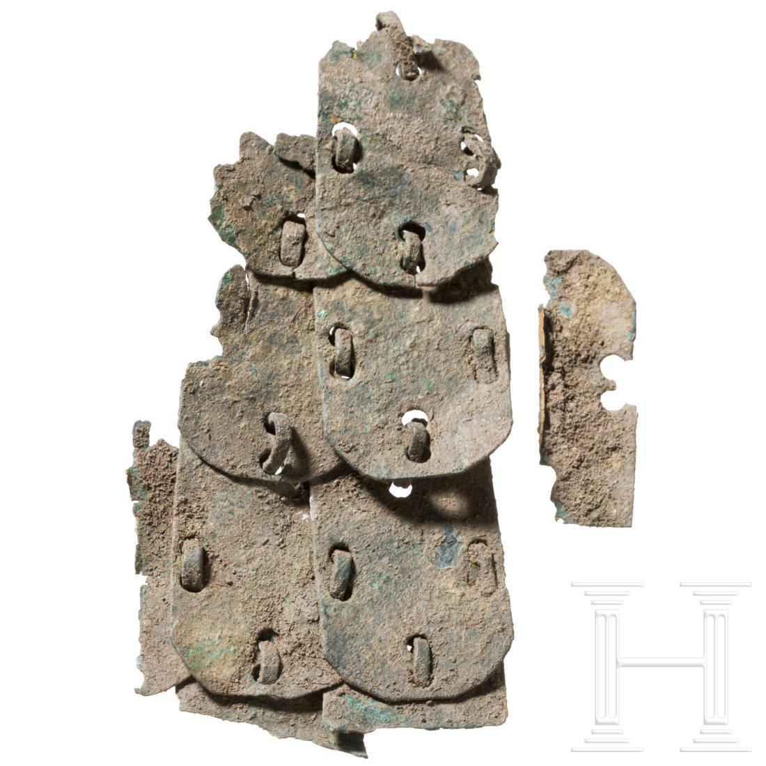 A fragment of a Roman lorica squamata, 2nd - 3rd: Segment of a lorica squamata consisting of nine bronze lamellas connected by wire rings. Four of the lamellas only partially preserved. With dark-green patina. Length 7 cm.Provenance: From a private c