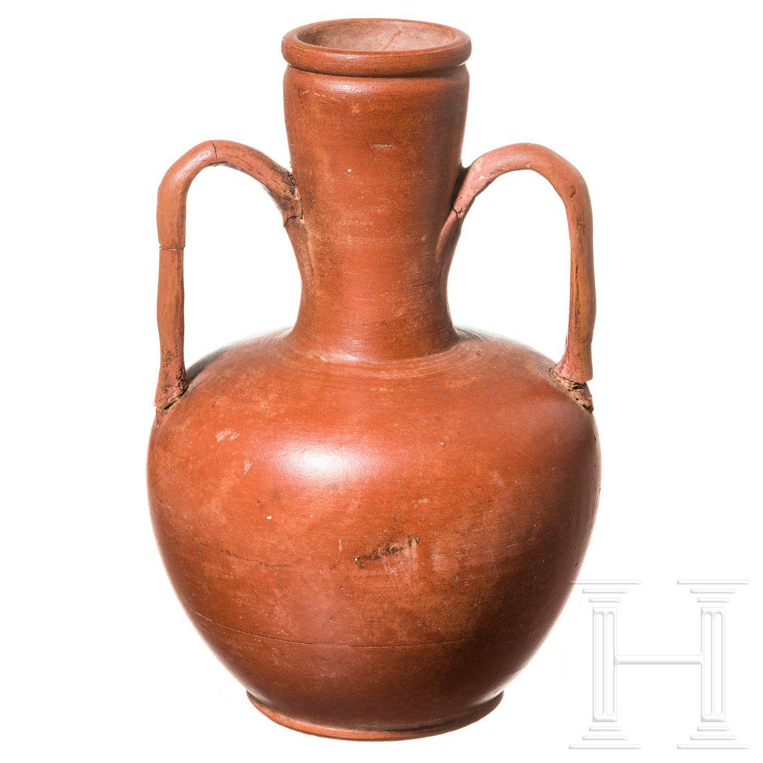 A Roman Terra sigillata jug, 2nd - 3rd century: Bottle with bulbous body, cylinder neck and two thin handles. Both handles broken and glued. Intact. Height 18.8 cm.Provenance: From a collection in North Germany.Condition: II -